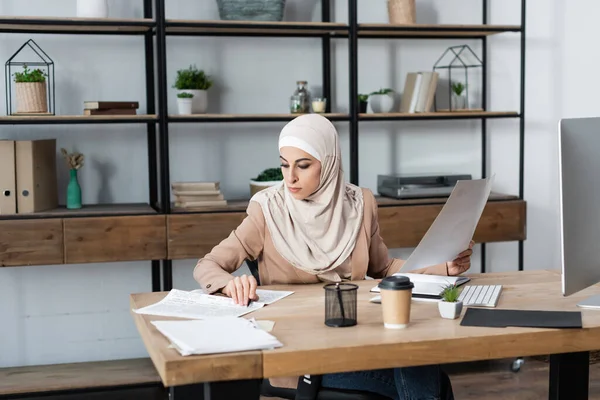 Young arabian woman working with newspaper and documents near computer monitor at home — Stock Photo