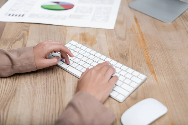 Cropped view of woman typing on keyboard near computer mouse and graphs on desk — Stock Photo
