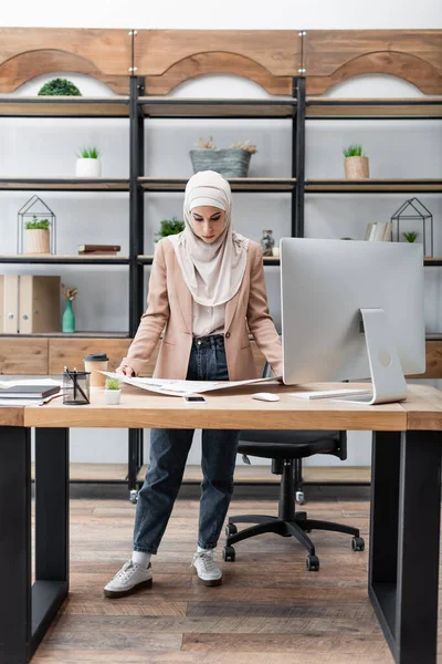 Vue complète de la femme musulmane regardant les documents près du bureau de travail à la maison — Photo de stock