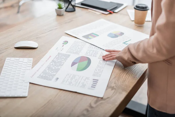 Cropped view of businesswoman near graphs, keyboard and coffee to go on work desk — Stock Photo