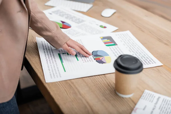 Partial view of businesswoman pointing at papers with analytics near takeaway drink on desk — Stock Photo