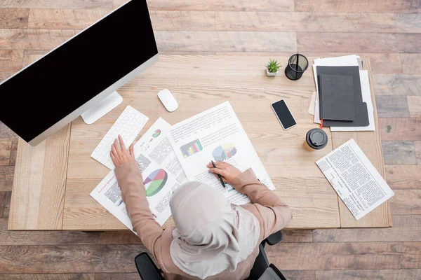 Ansicht der muslimischen Geschäftsfrau, die zu Hause mit Infografik und Computer arbeitet — Stockfoto