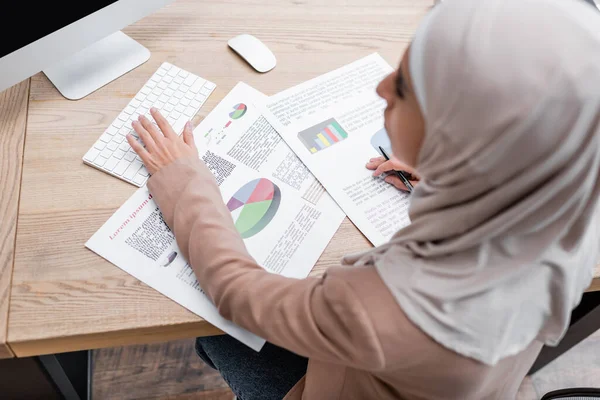 Overhead view of blurred muslim woman typing on keyboard while working with analytics at home — Stock Photo