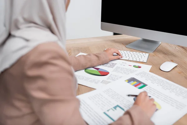 Vista parziale della donna musulmana offuscata che lavora con infografica e computer a casa — Foto stock
