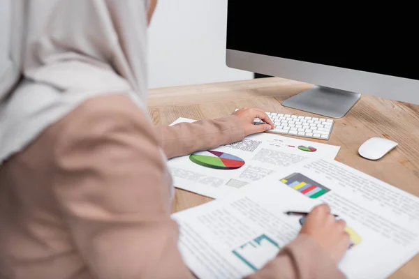 Partial view of blurred muslim woman working with infographics and computer at home — Stock Photo