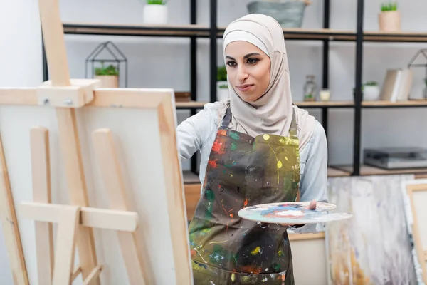 Joven mujer musulmana en lienzo y hijab dibujo sobre lienzo en casa - foto de stock