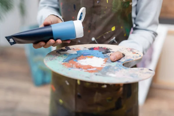 Vista recortada de la mujer borrosa sosteniendo tubo de pintura cerca de la paleta - foto de stock