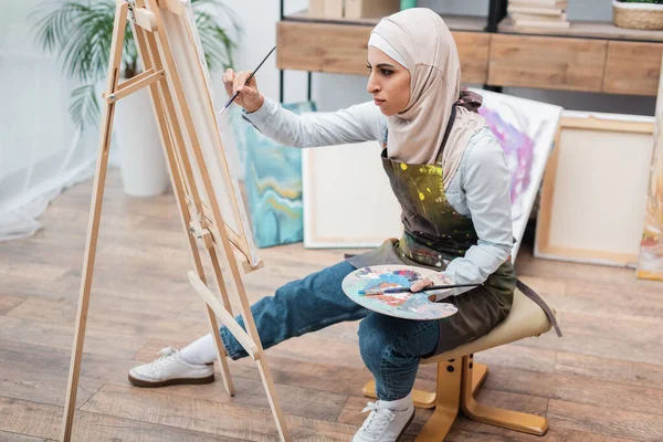 Visão comprimento total da mulher muçulmana desenho no cavalete em casa — Fotografia de Stock