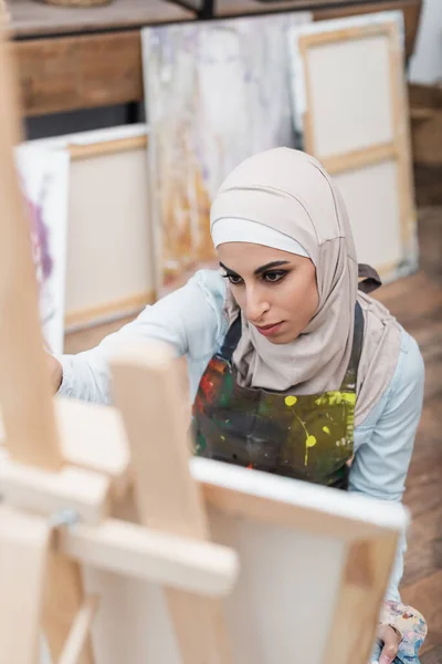 High angle view of arabian woman in hijab drawing on blurred easel at home — Stock Photo