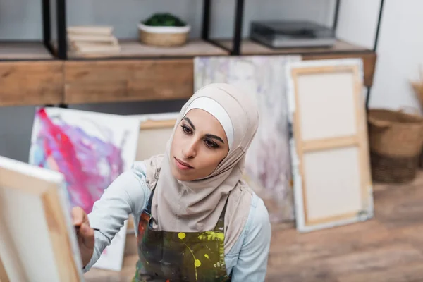 Joven musulmana mujer en hijab y delantal pintura en casa - foto de stock