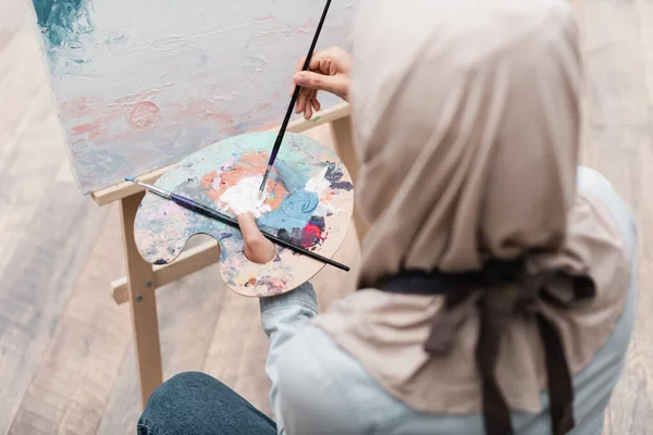 Blurred muslim woman with palette and paintbrushes drawing at home — Stock Photo