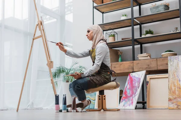 Vista lateral da mulher muçulmana desenho no cavalete em estúdio em casa — Fotografia de Stock