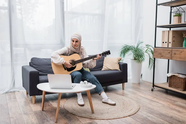 Cheerful muslim woman playing guitar during video lesson on laptop — Stock Photo