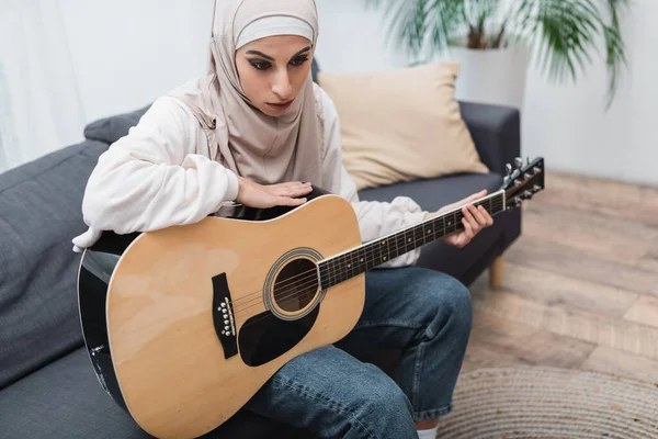 Mulher muçulmana com guitarra acústica sentado no sofá em casa — Fotografia de Stock