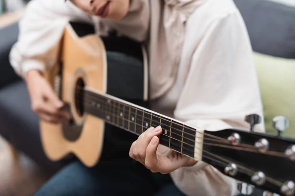 Vista cortada de mulher muçulmana desfocada tocando guitarra acústica em casa — Fotografia de Stock