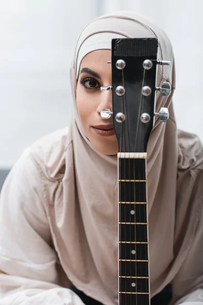 Araba donna in hijab guardando fotocamera vicino al collo della chitarra — Foto stock