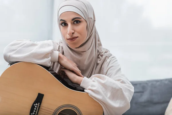 Jeune femme musulmane regardant la caméra près de la guitare acoustique — Photo de stock