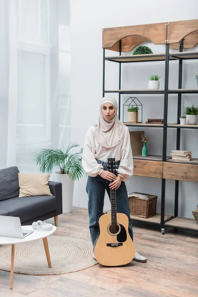 Полный вид мусульманской женщины с акустической гитарой в гостиной — стоковое фото