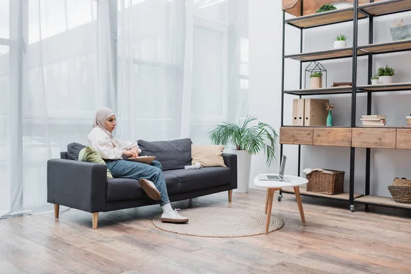 Araberin mit Schüssel Popcorn schaut Film auf Laptop im modernen Wohnzimmer — Stockfoto