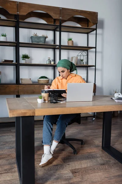 Studente musulmano che cerca nel notebook mentre impara vicino al computer portatile a casa — Foto stock