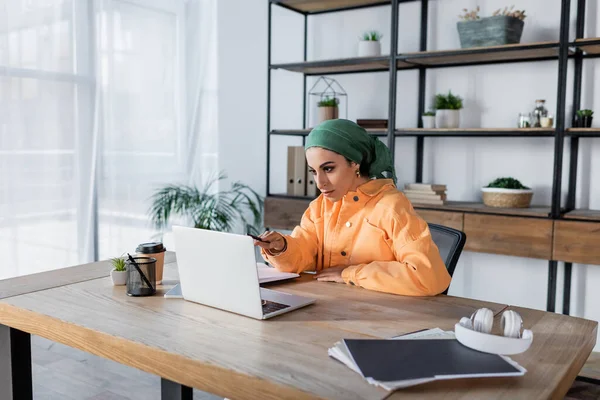 Muslim woman pointing with pen at laptop during online lesson at home — Stock Photo