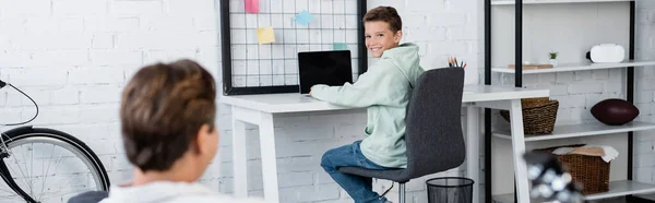 Lächelnder Junge mit Laptop neben verschwommenem Papa zu Hause, Banner — Stockfoto