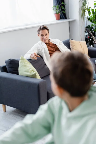 Padre señalando con el dedo cerca borrosa hijo en casa - foto de stock