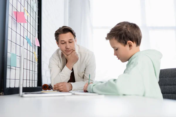 Preteen kid writing on notebook near laptop and dad at home — Stock Photo