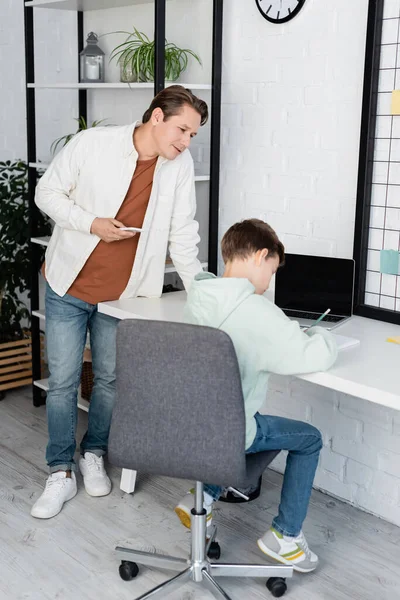 Man holding cellphone while child doing homework at home — Stock Photo