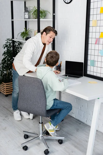 Man talking to son near notebook and laptop at home — Stock Photo