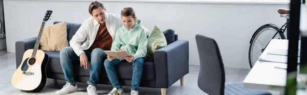 Garçon souriant lisant le livre près du parent sur le canapé à la maison, bannière — Photo de stock