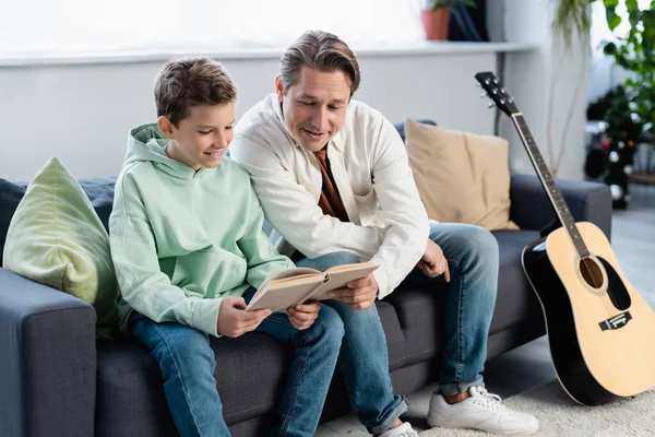 Padre e hijo alegre leyendo libro en el sofá - foto de stock
