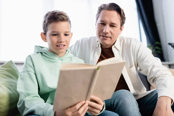 Preteen enfant et père lecture livre flou dans le salon — Photo de stock