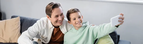 Positive parent and preteen son taking selfie on smartphone at home, banner — Stock Photo
