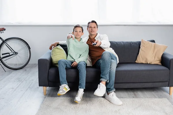 Fils excité pointant du doigt tout en regardant la télévision avec papa à la maison — Photo de stock