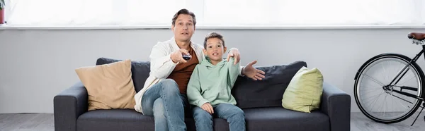 Aufgeregter Mann mit Fernbedienung schaut Film mit Sohn zu Hause, Banner — Stockfoto