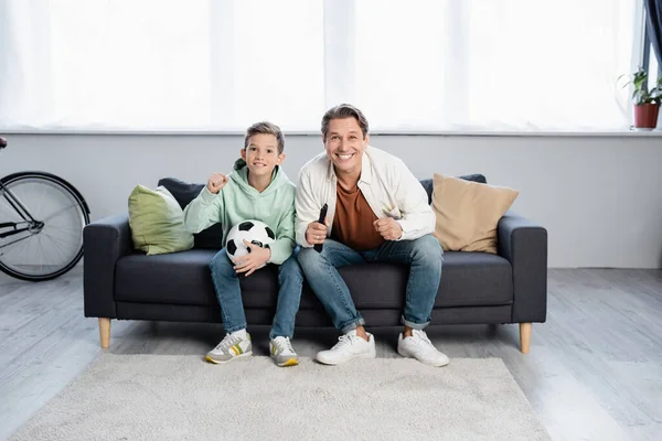 Excited father and son with football ball watching movie at home — Stock Photo