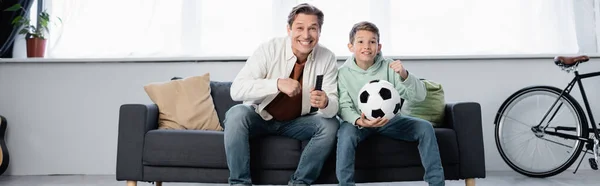 Захоплений батько і син дивиться футбольний матч вдома, банер — стокове фото