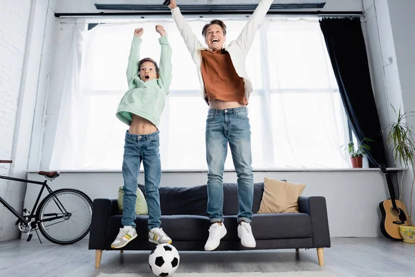 Cheerful father and son watching football match and jumping at home — Stock Photo