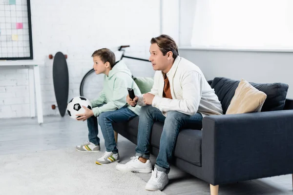 Focalisé homme avec télécommande regarder match de football près de son à la maison — Photo de stock