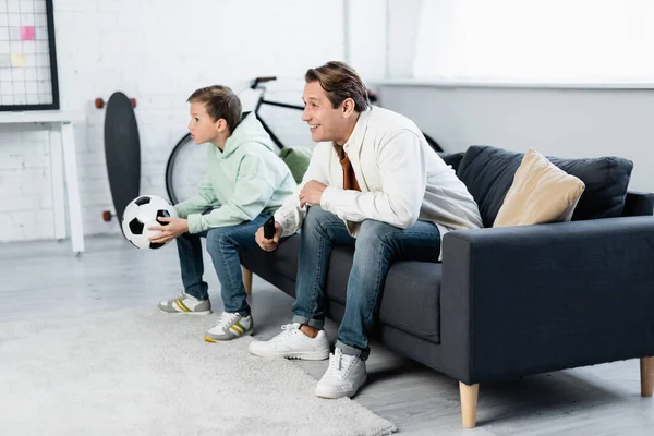 Padre positivo y niño viendo el partido de fútbol en el sofá - foto de stock