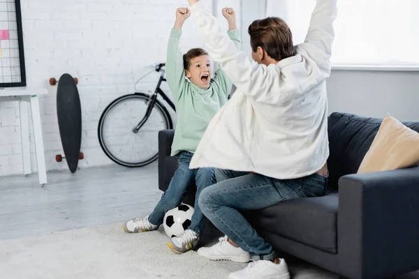 Boy and dad showing yes gesture near football ball at home — Stock Photo