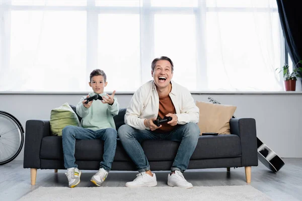 KYIV, UCRANIA - 11 de octubre de 2021: Hombre feliz jugando videojuegos con su hijo en casa - foto de stock