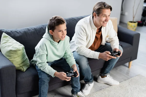 QUIIV, UCRÂNIA - OUTUBRO 11, 2021: Menino pré-adolescente alegre jogando videogame com o pai na sala de estar — Fotografia de Stock