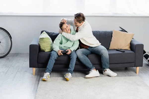 KYIV, UKRAINE - OCTOBER 11, 2021: Father touching son with joystick on couch at home — Stock Photo