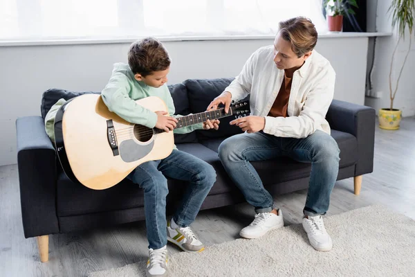 Père enseignant fils avec guitare acoustique à la maison — Photo de stock