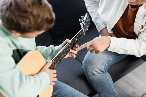 Mann zeigt mit Finger auf Kopf, während Sohn zu Hause Akustikgitarre spielt — Stockfoto