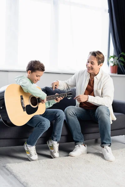 Papa positif pointant vers la guitare acoustique près de son à la maison — Photo de stock