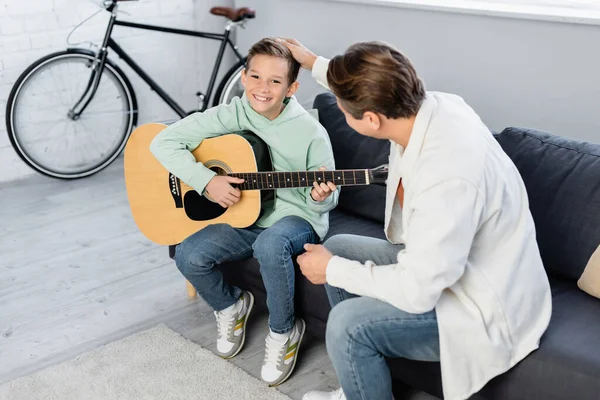 Mann berührt lächelnden Sohn zu Hause mit Akustikgitarre — Stockfoto