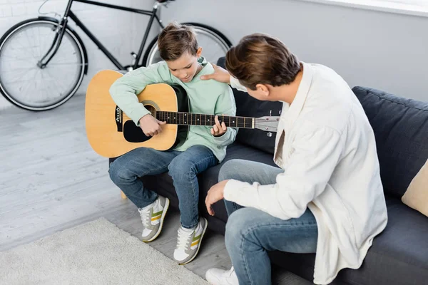 Menino tocando guitarra acústica perto do pai na sala de estar — Fotografia de Stock